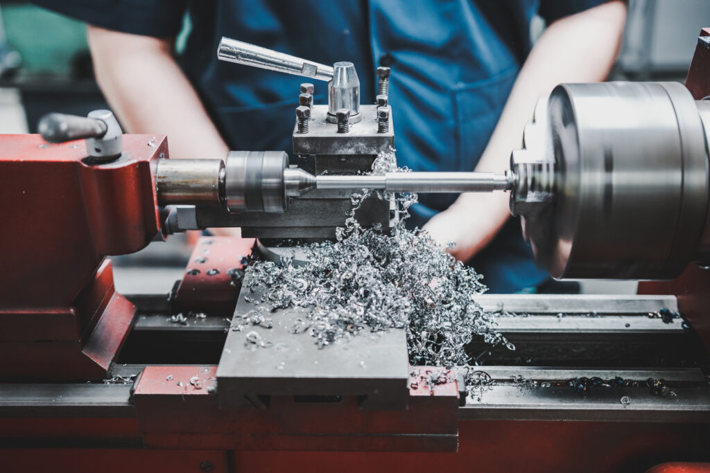 A metal lathe in operation with the operator standing behind the machine not wearing gloves